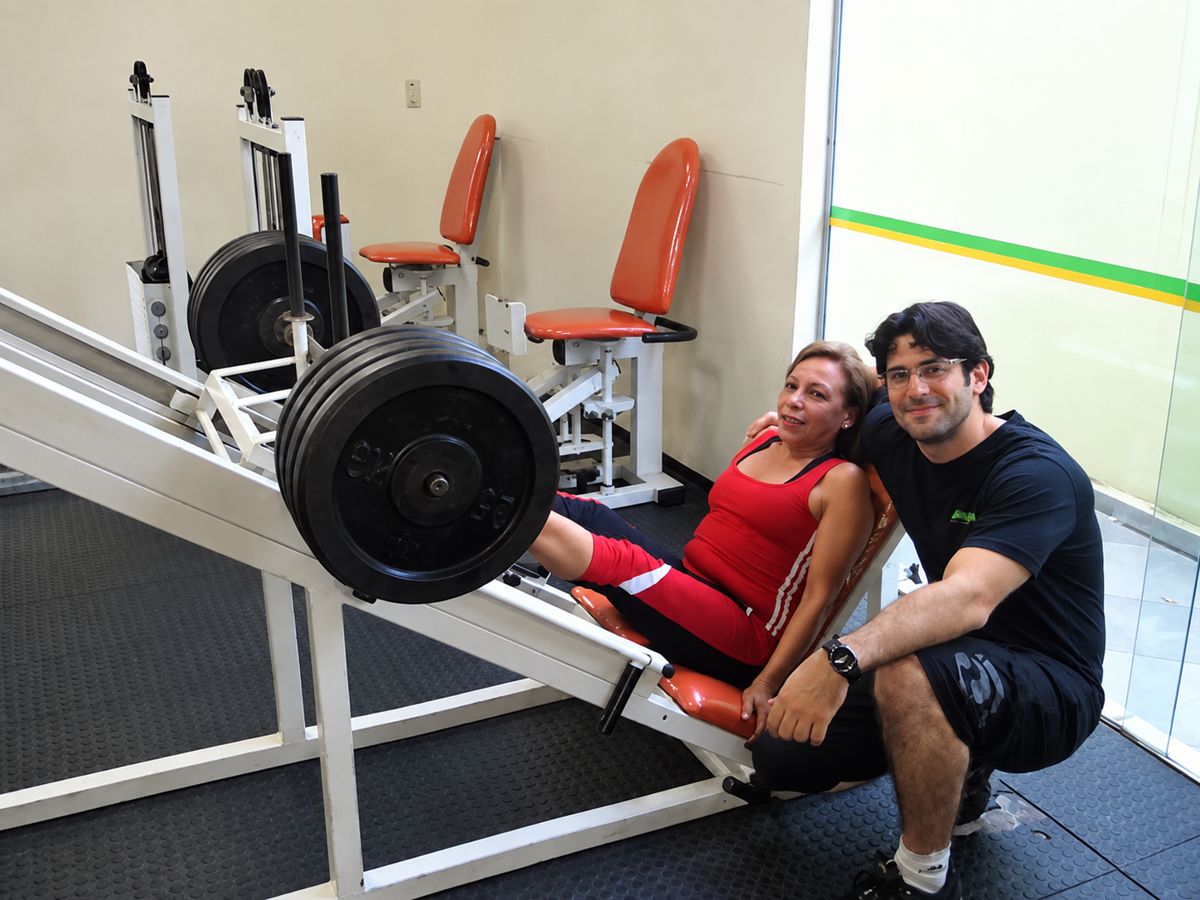 Aluna no leg press com Eduardo ao lado